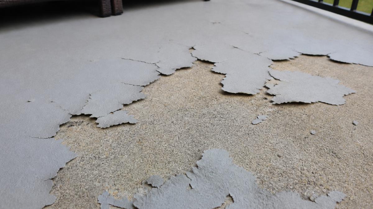 Close-up photograph of an outdoor concrete patio where the coating is peeling and flaking away from the surface, showing bare concrete underneath and curled coating edges